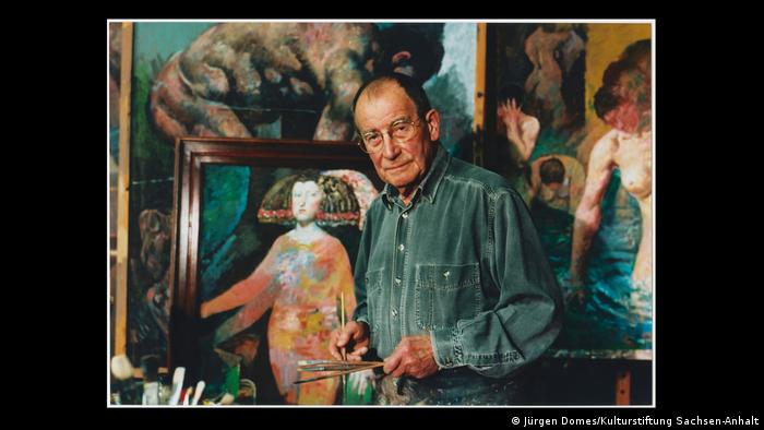 Ein Foto zeigt den DDR-Maler und Kulturfunktionär Willi Sitte mit Pinseln in der Hand vor einem seiner Bilder.