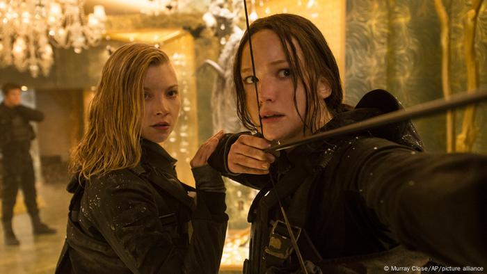 Film still 'The Hunger Games': Natalie Dormer as Cressida, left, and Jennifer Lawrence as Katniss Everdeen who is pulling a bow and arrow.