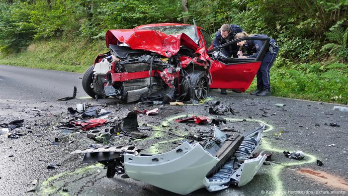 La police inspecte les restes mutilés d'une voiture rouge après un accident sur une route de campagne près de Siegen.