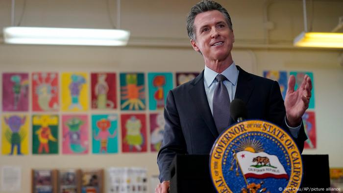 California governor Gavin Newsom speaks at a news conference in a middle school; there are paintings on the wall behind him