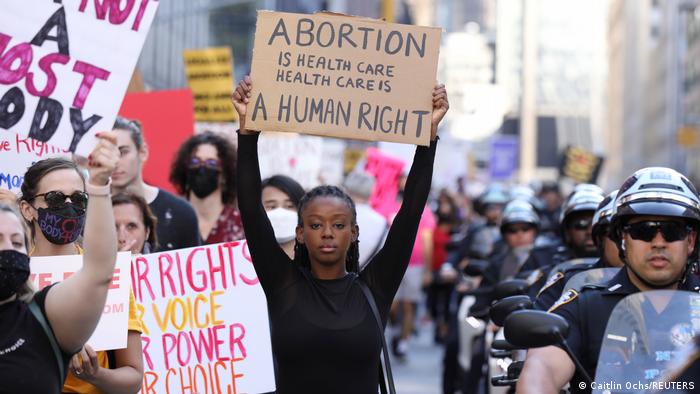 a young woman holds a sign that reads Abortion is healthcare, healthcare is a human right