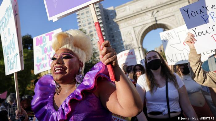 In New York, a protester wears a purple ruff and blonde beehive wig on the march while grasping a sign