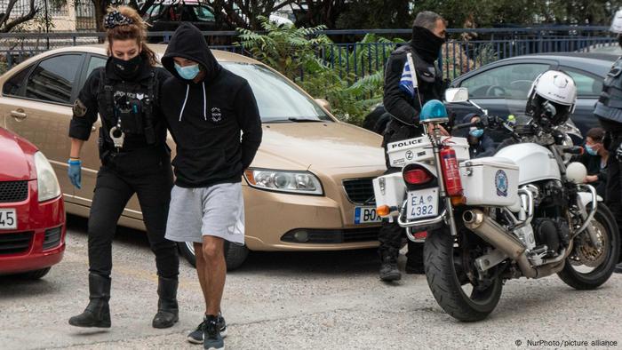 A police officer walks with a masked youth wearing black