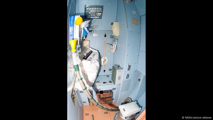 Toilet in ISS, lightr blue room with equipment