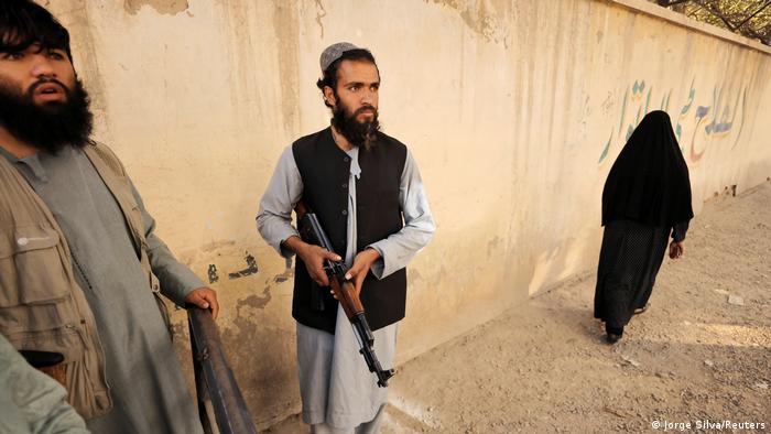 A Taliban soldier carrying a weapon as Afghans gather outside the passport office after Taliban officials announced they will start issuing passports to Afghan citizens again