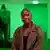 Sandra Mujinga, baldheaded woman looks into camera in a room lit eerily green, 