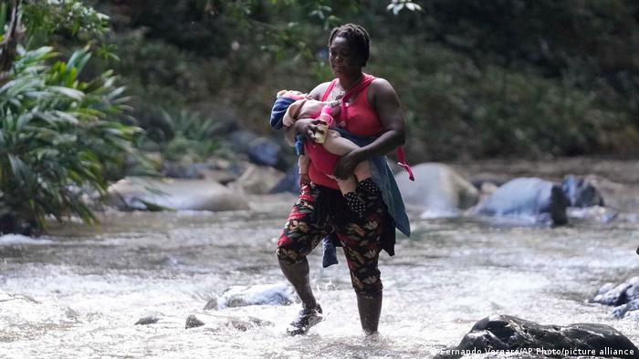 Una mujer migrante con su bebé en brazos cruza el río Acandí, en Colombia, en el Tapón de Darién