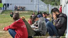 Mehrere Migranten sitzen auf einer Wiese vor Containern in der Zentralen Erstaufnahmeeinrichtung für Asylbewerber (ZABH) des Landes Brandenburg. Im Zuge der deutlich gestiegenen Registrierung von Migranten in Brandenburg informierte sich der Innenminister des Landes Brandenburg, Stübgen (CDU), vor Ort über die aktuelle Situation.