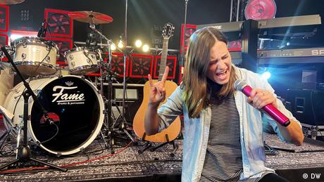 Woman holding microphone on a stage with drums and other instruments