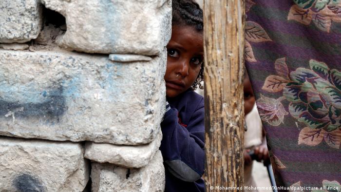  Child in Yemen looking out from behind a wll