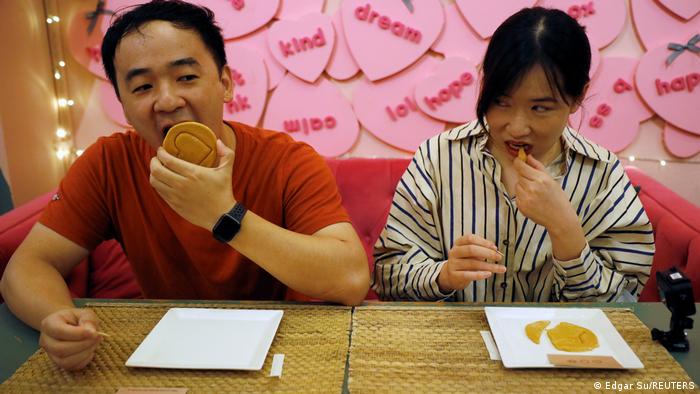 A man and a woman sit at a table, each with a large round candy.