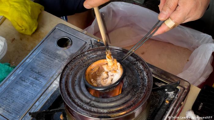 Sweets Game Squid : Mains tenant un récipient de sucre sur le brûleur