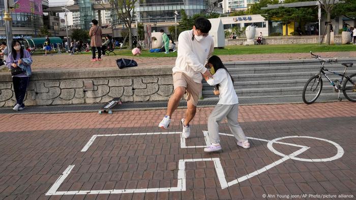 A man and a little girl lock arms on a squid-like diagram drawn on the ground in a playground.