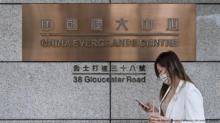 A woman looks at her phone as she walks past the China Evergrande Center in Hong Kong