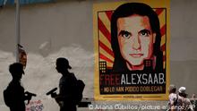 Pedestrians walk near a poster asking for the freedom of Colombian businessman and Venezuelan special envoy Alex Saab, in Caracas, Venezuela, Thursday, Sept 9, 2021. A court in Cape Verde ruled Tuesday that Saab, a businessman close to Venezuelan President Nicolas Maduro arrested last year in the West African country, can be extradited to the United States to face money-laundering charges. (AP Photo/Ariana Cubillos)