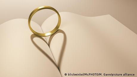A symbolic photo of a wedding ring on an open book, its shadow forming the shape of a heart