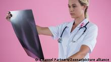 Female doctor looking at X-ray while standing against pink background || Modellfreigabe vorhanden