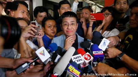 Journalist Maria Ressa surrounded by journalists with microphones and cellphones