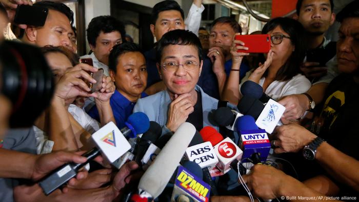Journalist Maria Ressa surrounded by journalists with microphones and cellphones