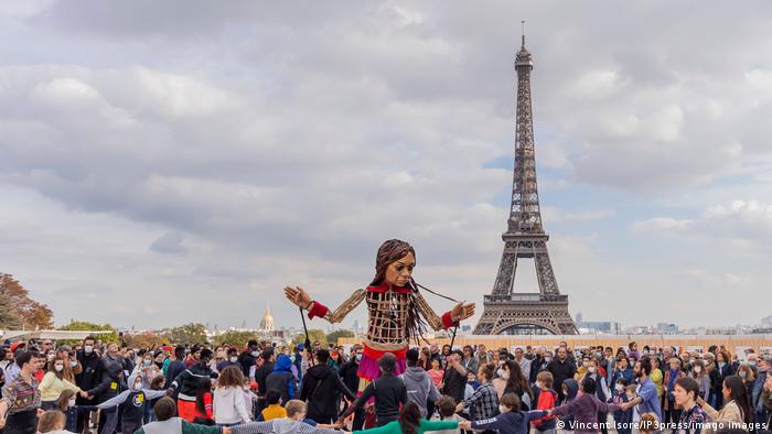 Huge doll surrounded by crowds, Eiffel Tower in the background