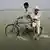 Ein junger Pakistani fährt mit dem Fahrrad durch das Wasser. Auf dem Gepäckträger sitzt ein älterer Pakistani (Foto: ap)