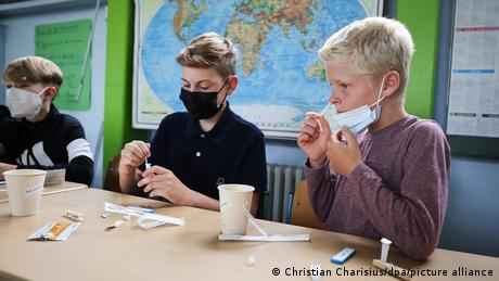 Three schoolchildren in Hamburg wearing masks, with testing kits.
