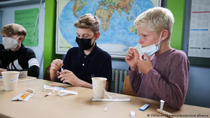 Tiga anak sekolah di Hamburg memakai masker, dengan alat tes.