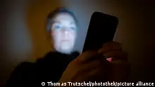 Symbolfoto zum Thema Handysucht: Eine Frau schaut in einem dunklen Raum auf ihr Smartphone. Berlin, 23.01.2021 || Modellfreigabe vorhanden