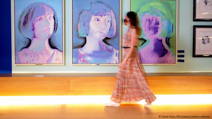 Eine Frau geht in einem Museum an drei Portrait-Gemälden vorbei