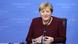 Merkel, de roupa vinho e colcar, sorri enquanto fala em um microfone de mesa. Ela está sentado e, ao fundo, há um painel azul com palavras desfocadas. Merkel, de roupa vinho e colcar, sorri enquanto fala em um microfone de mesa. Ela está sentado e, ao fundo, há um painel azul com palavras desfocadas.