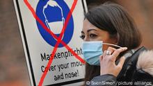 Wann endet die Maskenpflicht in Deutschland? Experten gehen davon aus, dass uns der Mundschutz noch eine Weile erhalten bleibt. Archivfoto: Junge Frau mit Mundschutz,Maske. Schild Maskenpflicht Maskenpflicht in Fussgaengerzonen und oeffentlichen Plaetzen in Muenchen am 11.11.2020. MODEL RELEASED!