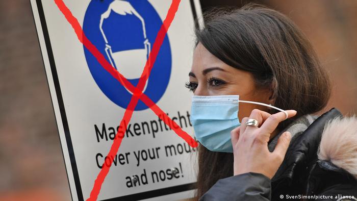 Woman with mask infront of sign where the call to cover mouth and nose is already crossed out