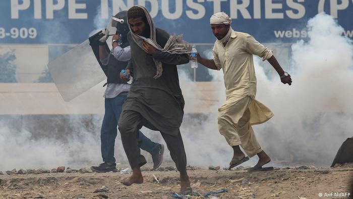 Tehreek-e-Labbaik Pakistan (TLP) supporters take cover as police use tear gas to disperse the crowd