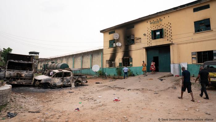 People walk past burned vehicles in front of a correctional facility in Owerri after 1,800 inmates were freed in a jailbreak in April