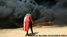 FILE PHOTO: A person wearing a Sudan's flag stand in front of a burning pile of tyres during a protest against prospect of military rule in Khartoum, Sudan October 21, 2021. REUTERS/Mohamed Nureldin Abdallah/File Photo