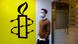 Amnesty symbol of barbed wire wrapped around a candle against a yellow background seen near the group's former Hong Kong office, with a man walking past it wearing a medical face mask Amnesty symbol of barbed wire wrapped around a candle against a yellow background seen near the group's former Hong Kong office, with a man walking past it wearing a medical face mask
