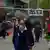 Pessoas de máscara em rua na China, com cartazes em chinês pendurados