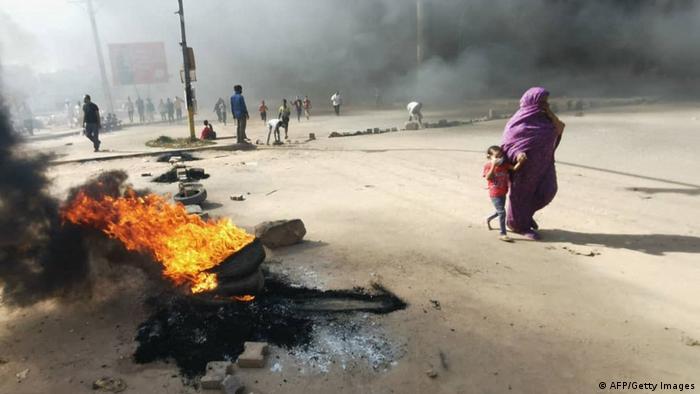 A Sudanese woman and child walk past as protesters burn tyres to block a road in 60th Street in the capital Khartoum, to denounce overnight detentions by the army of members of Sudan's government, on October 25, 2021