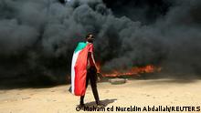 FILE PHOTO: A person wearing a Sudan's flag stand in front of a burning pile of tyres during a protest against prospect of military rule in Khartoum, Sudan October 21, 2021. REUTERS/Mohamed Nureldin Abdallah//File Photo