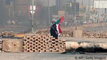A Sudanese demonstrator carrying a national flag walks by roadblocks set up by protesters on a street in the capital Khartoum, on October 26, 2021, to denounce a military coup that overthrew the transition to civilian rule. - Angry Sudanese stood their ground in street protests against a coup, as international condemnation of the military's takeover poured in ahead of a UN Security Council meeting. (Photo by AFP) (Photo by -/AFP via Getty Images)