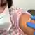 Руки у гумових рукавицях наклеюють на плече жінки пластир після вакцинації