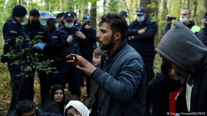 A group of migrants standing in a forest with border guards around them
