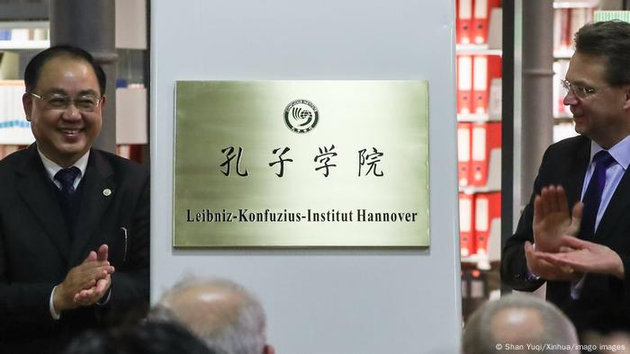 Chinesisch-deutsches Schild mit Aufschrift Leibnis-Konfuzius-Institut, daneben zwei Männer, die klatschen.