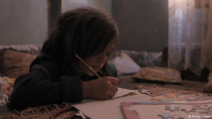 Ein Mädchen sitzt an einem Tisch und schreibt mit einem Stift einen Brief. 