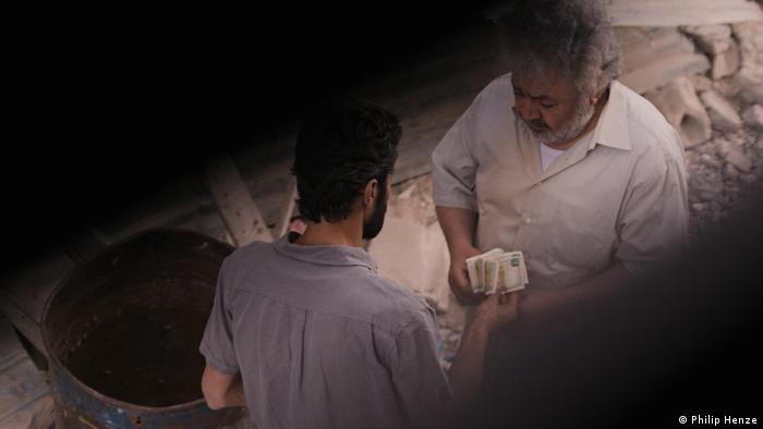 Die Kamera lässt uns an Talas Blick durch den Fensterspalt teilhaben: Zu sehen sind zwei syrische Männer, sie übergeben sich Geldscheine