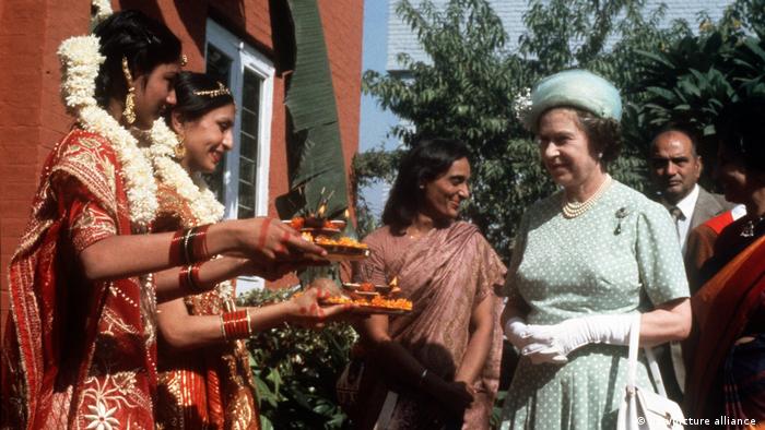 Ladies in traditional Indian clothing offer platters of food to the Queen.
