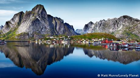 A fjord in Norway with a village and mountain reflected in the water