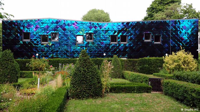 a building with a shimmering blue facsade in a park