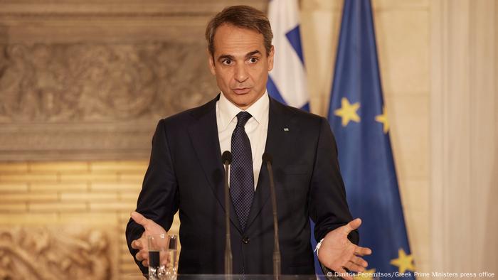 Greek Prime Minister Kyriakos Mitsotakis stands in front of a microphone during a press conference.