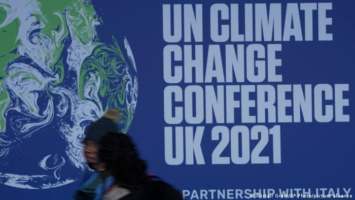 Attendees walk past a banner at the venue where COP climate conference will be held in Glasgow, Scotland